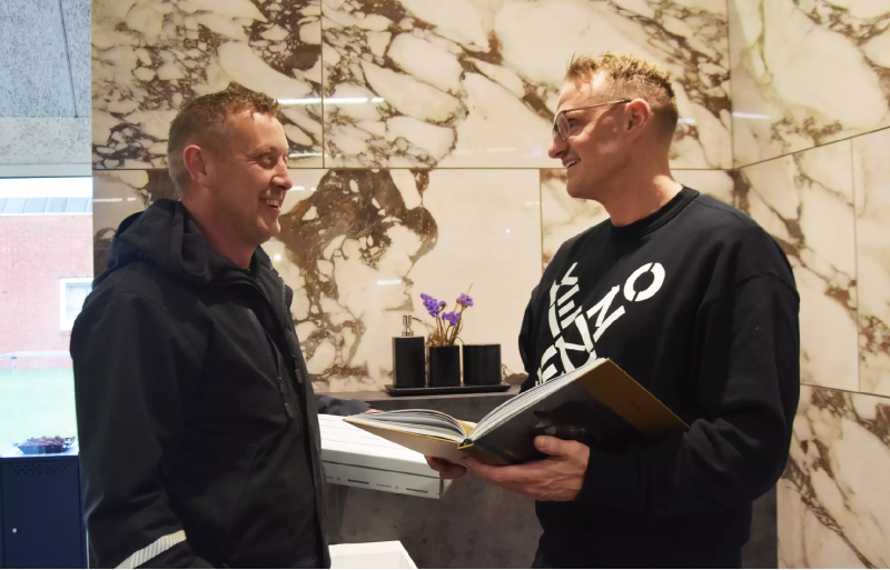 Professionel rådgivning hos Idegaarden – Få hjælp til dine projekter med vores ekspertteam. To medarbejdere fra Idegaarden diskuterer et projekt foran en væg med marmorfliser.